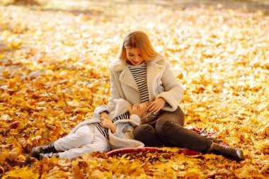 Güzel anne ve kızı, açık bir Ekim günü güneşli bir parkta canlı sonbahar yapraklarında neşeyle oynuyorlar. Aile Günü.