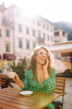 Karadağ 'ın Kotor kentinde sıcak bir kafede kahve içen genç bir kadın, güneşli bir öğleden sonra etrafı tarihi mimariyle çevrili. Yiyecek ve içecek..