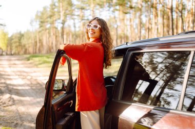 Öğleden sonra güneşli bir günde sakin bir orman ortamında arabasının yanında eğlenen genç bir kadın. Yaz gezisi. Yaşam tarzı, seyahat, turizm, doğa, aktif yaşam.