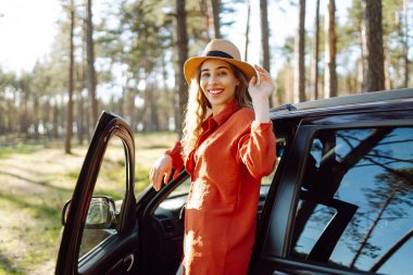 Öğleden sonra güneşli bir günde sakin bir orman ortamında arabasının yanında eğlenen genç bir kadın. Yaz gezisi. Yaşam tarzı, seyahat, turizm, doğa, aktif yaşam.