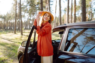 Öğleden sonra güneşli bir günde sakin bir orman ortamında arabasının yanında eğlenen genç bir kadın. Yaz gezisi. Yaşam tarzı, seyahat, turizm, doğa, aktif yaşam.