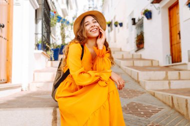 Güzel gezgin kadın eski kasabada güzel bir yürüyüşün tadını çıkarıyor. O güzel parlak bir elbise ve bir sırt çantası giyiyor. Yaşam tarzı kavramı, tatil, moda, seyahat.