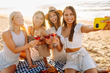 Okyanus kenarında güneşli bir öğleden sonra selfie çekerken ve içki içerken sahilde toplanan dört güzel bayan arkadaş. - Evet. Tatiller, doğa, rahatlama konsepti.