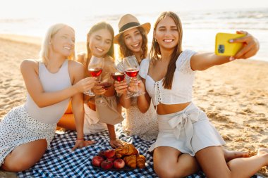 Okyanus kenarında güneşli bir öğleden sonra selfie çekerken ve içki içerken sahilde toplanan dört güzel bayan arkadaş. - Evet. Tatiller, doğa, rahatlama konsepti.