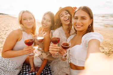 Okyanus kenarında güneşli bir öğleden sonra selfie çekerken ve içki içerken sahilde toplanan dört güzel bayan arkadaş. - Evet. Tatiller, doğa, rahatlama konsepti.