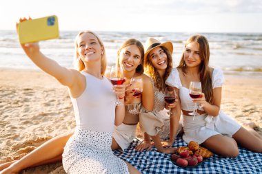 Okyanus kenarında güneşli bir öğleden sonra selfie çekerken ve içki içerken sahilde toplanan dört güzel bayan arkadaş. - Evet. Tatiller, doğa, rahatlama konsepti.