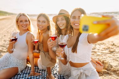Okyanus kenarında güneşli bir öğleden sonra selfie çekerken ve içki içerken sahilde toplanan dört güzel bayan arkadaş. - Evet. Tatiller, doğa, rahatlama konsepti.