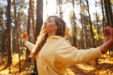 Bir kadın, sonbaharda yapraklar ve uzun ağaçlarla çevrili güneşli bir ormanda yoga yapıyor. Heather yaşam tarzı.