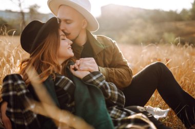 Çiftler, sıcak bir sonbahar öğleden sonrasında dağlarda bir tarlada otururken altın güneş ışığında kucaklaşırlar. Romantik randevu doğanın romantizm ilişkileri kavramında.