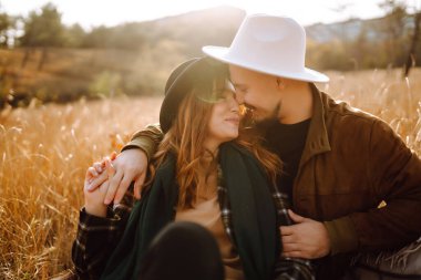 Çiftler, sıcak bir sonbahar öğleden sonrasında dağlarda bir tarlada otururken altın güneş ışığında kucaklaşırlar. Romantik randevu doğanın romantizm ilişkileri kavramında.