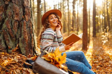 Bir kadın, düşen yaprakların üzerinde bisikletinin yanında otururken, sonbahar boyunca huzurlu bir ormanda kitap okumaktan hoşlanır.