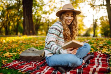 Genç bir kadın gün batımında parkta sonbahar yapraklarıyla çevrili sakin bir gölün kenarında kitap okumaktan hoşlanır. Rahatlama, keyif alma, doğayla baş başa kalma..