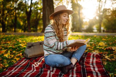 Genç bir kadın gün batımında parkta sonbahar yapraklarıyla çevrili sakin bir gölün kenarında kitap okumaktan hoşlanır. Rahatlama, keyif alma, doğayla baş başa kalma..