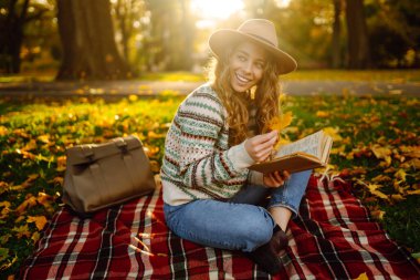 Genç bir kadın gün batımında parkta sonbahar yapraklarıyla çevrili sakin bir gölün kenarında kitap okumaktan hoşlanır. Rahatlama, keyif alma, doğayla baş başa kalma..