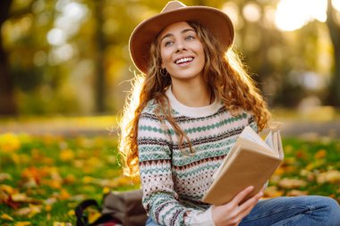 Genç bir kadın gün batımında parkta sonbahar yapraklarıyla çevrili sakin bir gölün kenarında kitap okumaktan hoşlanır. Rahatlama, keyif alma, doğayla baş başa kalma..