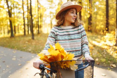 Bir kadın altın sonbahar ormanında bisiklet sürerken öğleden sonra güneş ışığında renkli yapraklarla dolu bir sepetin tadını çıkarıyor. Etkin yaşam biçimi.
