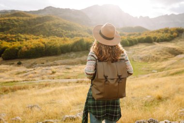 Bir kadın kayalık arazide duruyor, canlı sonbahar ağaçları ve dağlara bakıyor. Çevre turizmi. Etkin yaşam biçimi.