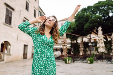 Yeşil elbiseli bir kadın, Akdeniz 'in büyüleyici tarihi meydanında güneşli bir günün tadını çıkarıyor. Yüksek binalara ve saat kulesine bakıyor. Moda, tarz, turizm konsepti.