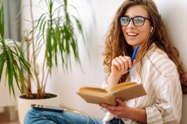 Kıvırcık saçlı ve gözlüklü genç bir kadın elinde bitkilerle çevrili bir kitap ve kalemle gülümsüyor. - Evet. Ev hayatı işte. Rahatla ve rahatla.
