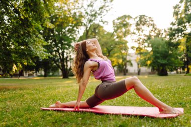 Bir kadın sıcak bir öğleden sonra minder ve ağırlık kullanırken güneşli bir parkta yoga yapıyor. - Evet. Sağlıklı yaşam tarzı, spor. Fitness.