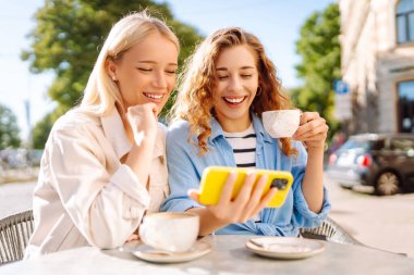 Arkadaşlar açık bir kafede keyifli bir anı paylaşırlar, sıcak öğleden sonra ışığında kahve yudumlarlar ve selfie çekerler, birlikte kalıcı anılar yaratırlar. Moda, güzellik, blog, turizm.