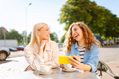 Arkadaşlar açık bir kafede keyifli bir anı paylaşırlar, sıcak öğleden sonra ışığında kahve yudumlarlar ve selfie çekerler, birlikte kalıcı anılar yaratırlar. Moda, güzellik, blog, turizm.