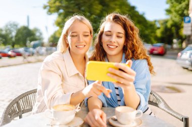 Arkadaşlar açık bir kafede keyifli bir anı paylaşırlar, sıcak öğleden sonra ışığında kahve yudumlarlar ve selfie çekerler, birlikte kalıcı anılar yaratırlar. Moda, güzellik, blog, turizm.