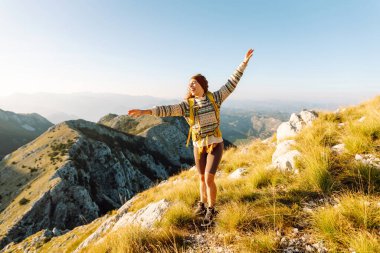 Neşeli bir yürüyüşçü dingin eteklerde güneşli bir öğleden sonra bir dağ zirvesinden nefes kesici manzaranın tadını çıkarır. Doğa, aktif yaşam, seyahat.
