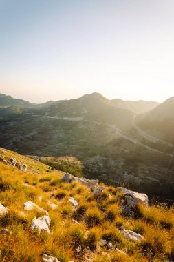 Güneş dağlık bir arazide yükselir, kayalık tepelerde ve aşağıdaki yemyeşil vadilerde ılık altın bir parıltı bırakır, dingin ve nefes kesici bir manzara yaratır..