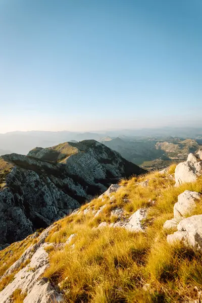 Güneş dağlık bir arazide yükselir, kayalık tepelerde ve aşağıdaki yemyeşil vadilerde ılık altın bir parıltı bırakır, dingin ve nefes kesici bir manzara yaratır..