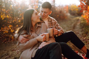 Bir çift, canlı yeşillikler ve yumuşak güneş ışığıyla renkli bir ormanda sakin bir sonbahar gününde neşeli bir anın tadını çıkarıyor. Gençlik, aşk ve yaşam tarzı kavramı.