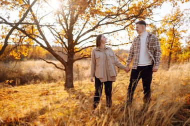 Bir çift, canlı yeşillikler ve yumuşak güneş ışığıyla renkli bir ormanda sakin bir sonbahar gününde neşeli bir anın tadını çıkarıyor. Gençlik, aşk ve yaşam tarzı kavramı.