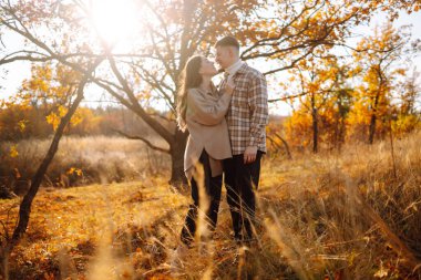 Bir çift, canlı yeşillikler ve yumuşak güneş ışığıyla renkli bir ormanda sakin bir sonbahar gününde neşeli bir anın tadını çıkarıyor. Gençlik, aşk ve yaşam tarzı kavramı.