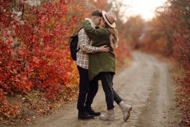 Bir çift, canlı yeşillikler ve yumuşak güneş ışığıyla renkli bir ormanda sakin bir sonbahar gününde neşeli bir anın tadını çıkarıyor. Gençlik, aşk ve yaşam tarzı kavramı.