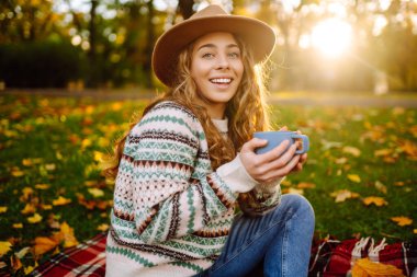 Sonbahar boyunca parkta, renkli yapraklarla çevrili sıcak bir içeceğin keyfini çıkaran genç bir bayanla sıcak öğleden sonra pikniği. Dinlenme, rahatlama kavramı. Yaşam biçimi.