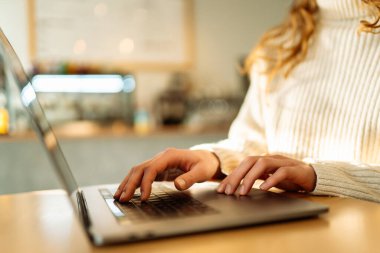 Öğleden sonra sıcak ve davetkar bir atmosferle çevrili bir kafede dizüstü bilgisayarda yazı yazan biri. Teknoloji, internet, serbest çalışan, çevrimiçi eğitim, alışveriş.