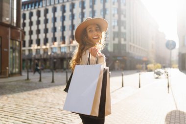 Genç bir kadın güneşli bir günde elinde birden fazla torbayla şık bir şehir bölgesinde alışveriş yapmaktan hoşlanıyor. Satış kavramı, alışveriş.
