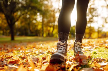Güneş ışığı ağaçların arasından süzülerek canlı sonbahar yapraklarının arasında duruyor, yürüyüş botlarını gösteriyor ve mevsimin güzelliğinin tadını çıkarıyor. Açık hava yürüyüşü.