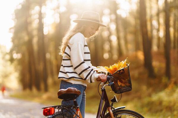 Радостная женщина едет на велосипеде по живописной лесной дорожке, украшенной осенними листьями в солнечный день. Активный образ жизни.
