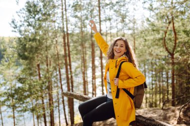 Sarı ceketli neşeli genç bir kadın sonbaharda ağaçtan bir merdiven boyunca gölün kenarında güneşli bir günün tadını çıkarıyor. Seyahatler. Etkin yaşam biçimi.