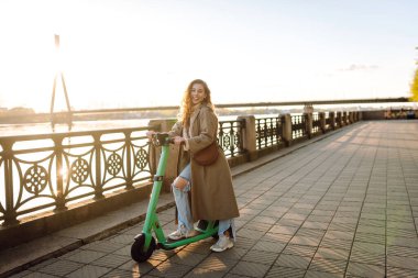 Genç bir kadın, deniz kenarında manzaralı gezintide elektrikli scooterla güneşli bir günün tadını çıkarıyor. Eko-bilinçli taşıma. Seyahat, turizm konsepti.