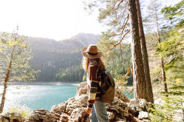 Şık bir şapka ve süveter giyen gezgin kadın güneşli sonbahar havasında dağlarda manzaranın tadını çıkarıyor. Çevre turizmi. Etkin yaşam biçimi.