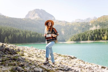 Şık bir şapka ve süveter giyen gezgin kadın güneşli sonbahar havasında dağlarda manzaranın tadını çıkarıyor. Çevre turizmi. Etkin yaşam biçimi.