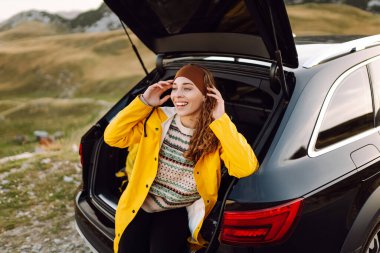 Neşeli bir gezgin öğleden sonra güneş ışığında park halindeki bir cipin bagajında otururken manzaralı bir dağ manzarasının tadını çıkarıyor. Arabayla seyahat etmek.. 