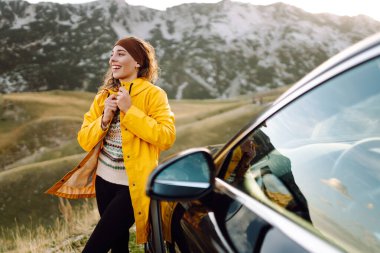 Neşeli bir gezgin öğleden sonra güneş ışığında park halindeki bir cipin bagajında otururken manzaralı bir dağ manzarasının tadını çıkarıyor. Arabayla seyahat etmek.. 