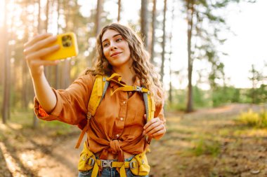 Doğadaki selfie. Güneşli bir ormanda yürürken fotoğrafını çeken güzel bir kadın.. 