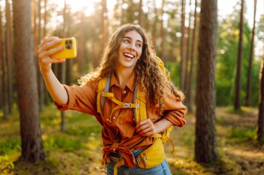 Doğadaki selfie. Güneşli bir ormanda yürürken fotoğrafını çeken güzel bir kadın.. 