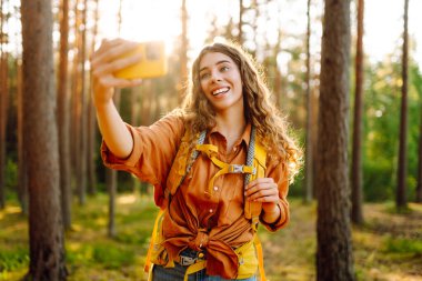 Doğadaki selfie. Güneşli bir ormanda yürürken fotoğrafını çeken güzel bir kadın.. 