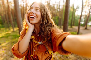 Doğadaki selfie. Güneşli bir ormanda yürürken fotoğrafını çeken güzel bir kadın.. 