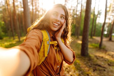 Doğadaki selfie. Güneşli bir ormanda yürürken fotoğrafını çeken güzel bir kadın.. 